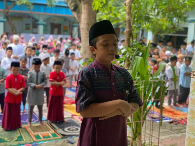 Seorang anak berdiri di depan barisan anak-anak yang sedang melaksanakan salat.